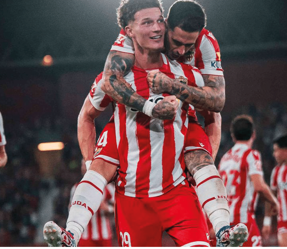 Jugadores de f tbol con uniforme a rayas rojas y blancas celebran en un estadio durante un partido nocturno. Descripci n generada con IA