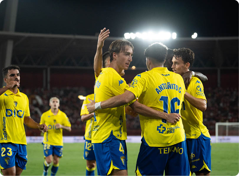 People wearing yellow and blue sports uniforms are celebrating on a soccer field under bright stadium lights. Descripci n generada con IA
