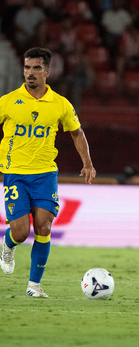 A person wearing a yellow and blue soccer uniform is running on a grass field while controlling a soccer ball. Descripci n generada con IA