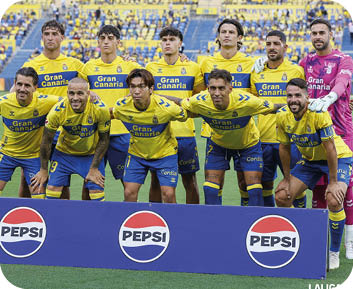 Un grupo de personas vestidas con uniformes deportivos amarillos y azules posan juntas en un campo de f tbol con un cartel de Pepsi al frente. Descripci n generada con IA