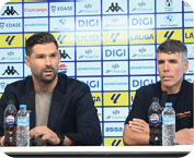 Dos personas sentadas en una mesa con micr fonos frente a un fondo con logotipos de patrocinadores durante una conferencia de prensa. Descripci n generada con IA