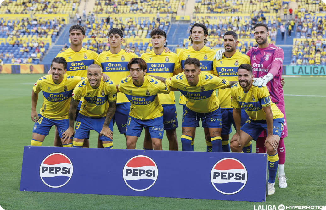 Un grupo de personas con uniformes deportivos amarillos y azules posan en un campo de f tbol frente a un cartel con el logo de Pepsi en un estadio con gradas llenas. Descripci n generada con IA