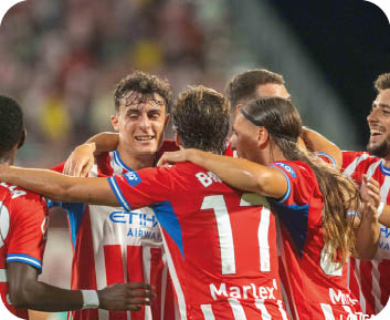 Un grupo de personas con uniformes deportivos rojos y blancos celebran abraz ndose en un ambiente de estadio. Descripci n generada con IA