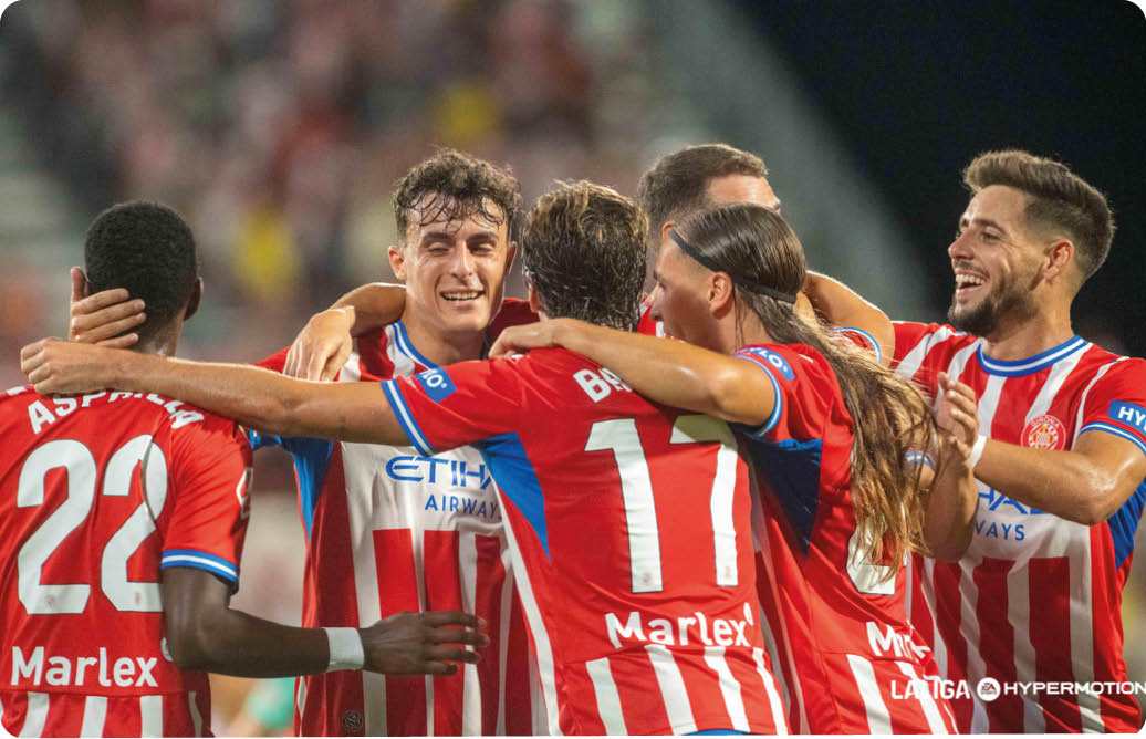 Un grupo de adultos con uniformes deportivos rojos y blancos celebran abrazados en un estadio. Descripci n generada con IA
