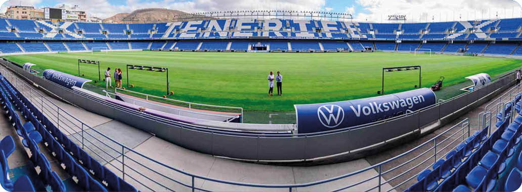 Gradas vac as de un estadio con asientos azules y una barandilla met lica en el centro. Descripci n generada con IA