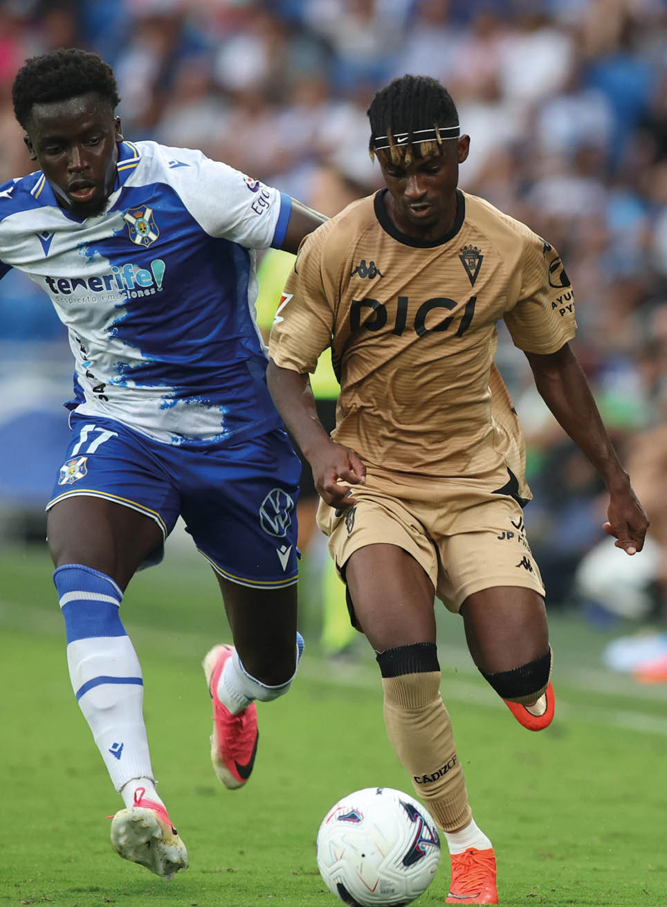 A person wearing a gold sports uniform and bright orange cleats is controlling a soccer ball on a grassy field during a game. Descripci n generada con IA