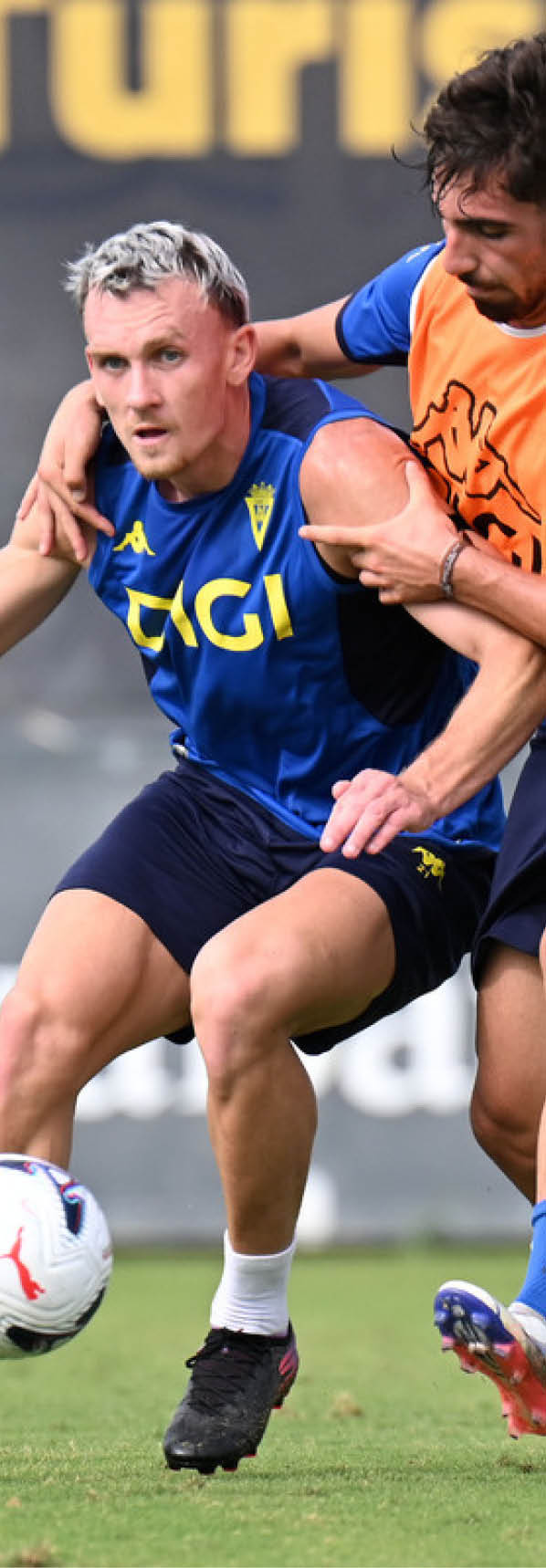 Dos adultos con ropa deportiva est n disputando un bal n de f tbol en un campo mientras uno intenta proteger la pelota del otro. Descripci n generada con IA