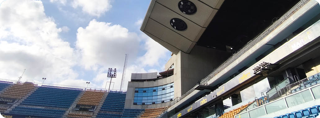 Estadio deportivo con gradas vac as bajo un cielo parcialmente nublado y una estructura met lica grande que sobresale sobre las gradas. Descripci n generada con IA