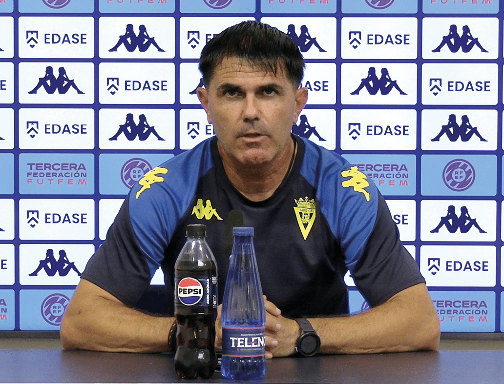 Persona con camiseta deportiva azul y negra sentada frente a un micr fono en una conferencia de prensa con botellas de Pepsi y agua sobre la mesa y un fondo con logotipos deportivos. Descripci n generada con IA