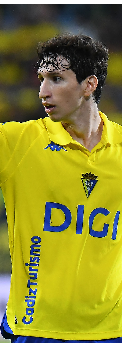 A person wearing a yellow sports jersey with blue text is pointing or gesturing with their arm extended. Descripci n generada con IA