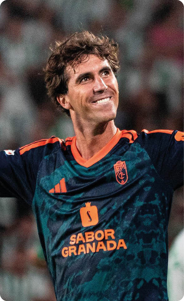 Una persona con camiseta deportiva azul y naranja levanta los brazos celebrando en un estadio con p blico desenfocado al fondo. Descripci n generada con IA