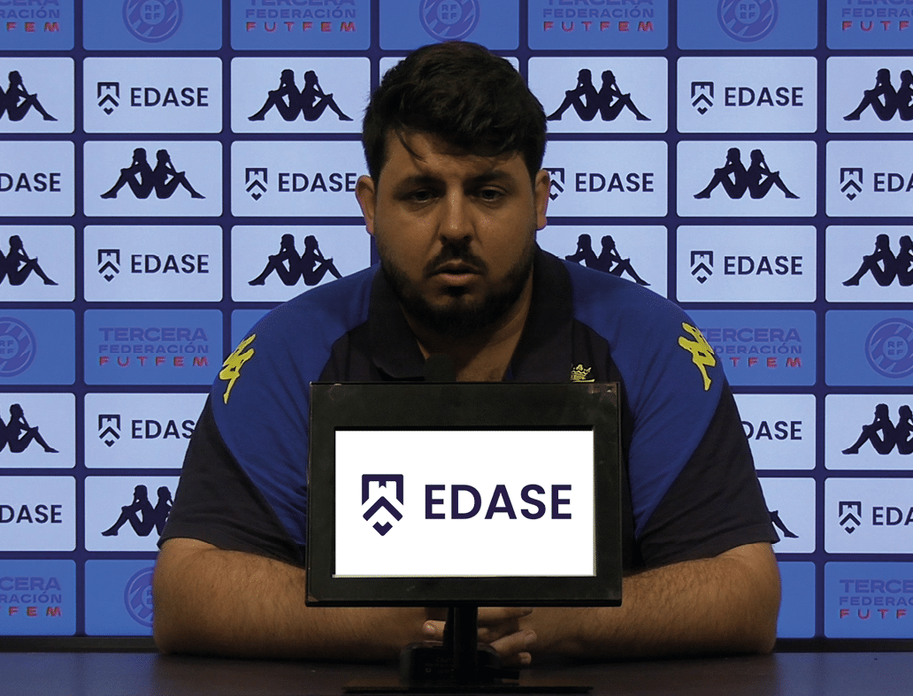 Una persona con camiseta azul y negra est sentada frente a un micr fono con un fondo de paneles publicitarios que muestran los logos de EDASE y Kappa.  Descripci n generada con IA