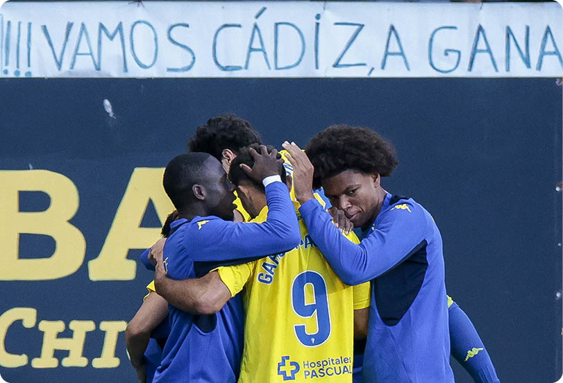 People in sports uniforms are celebrating together on a field with a banner in the background. Descripci n generada con IA